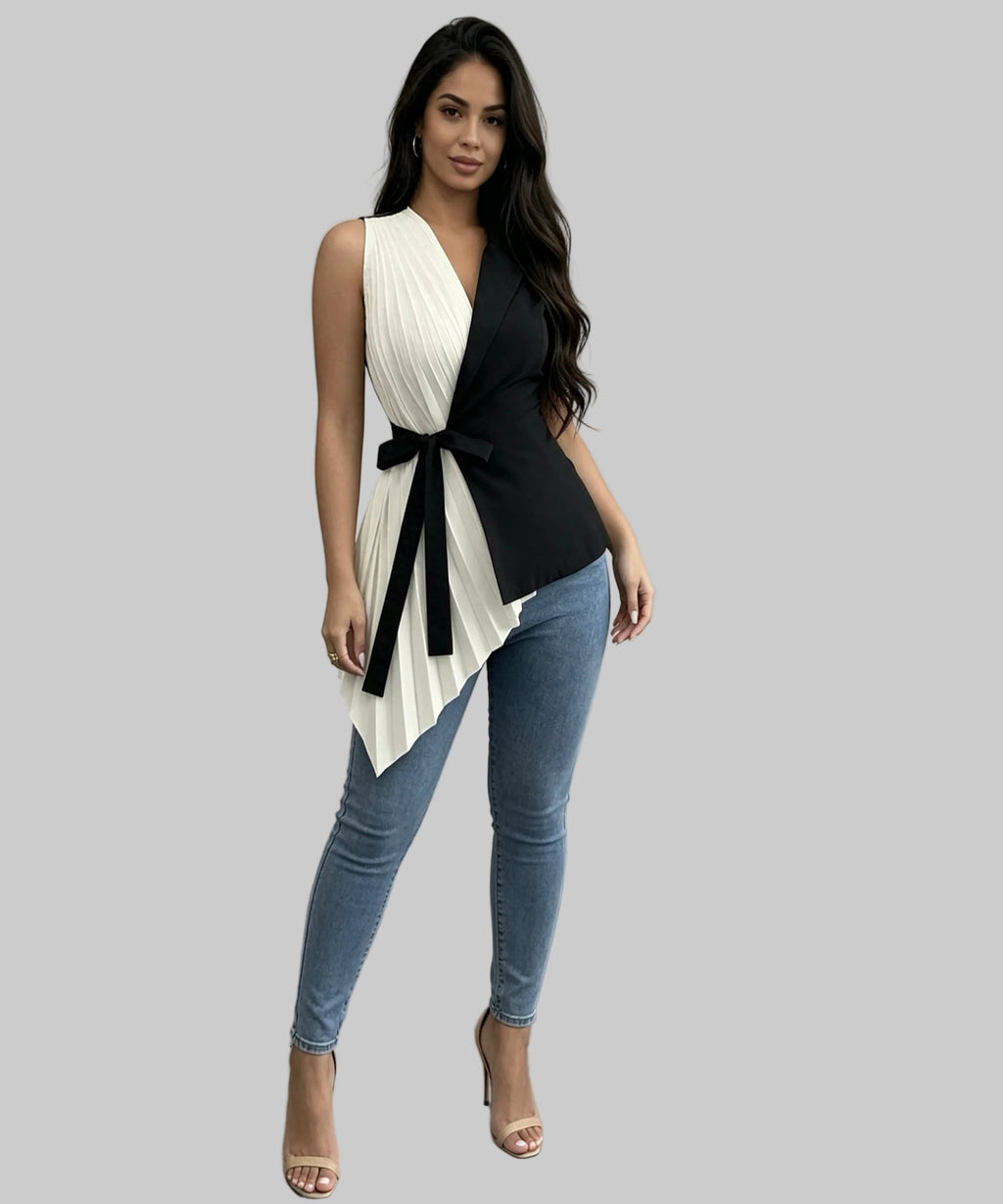 Woman wearing a black and white sleeveless top with a bow and blue jeans against a plain background