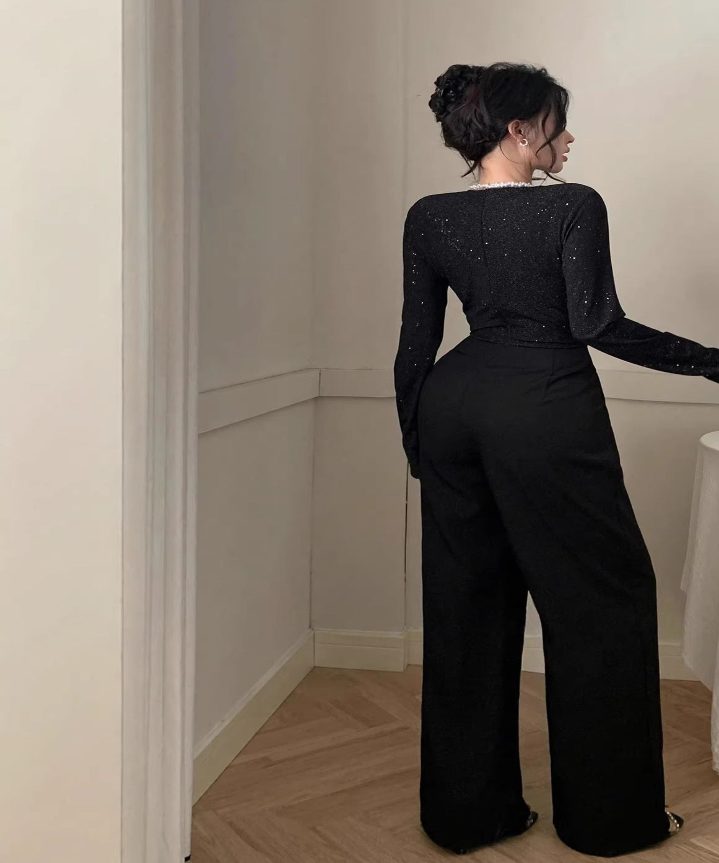 Woman in a black outfit standing near a table with a vase of flowers and candles.
