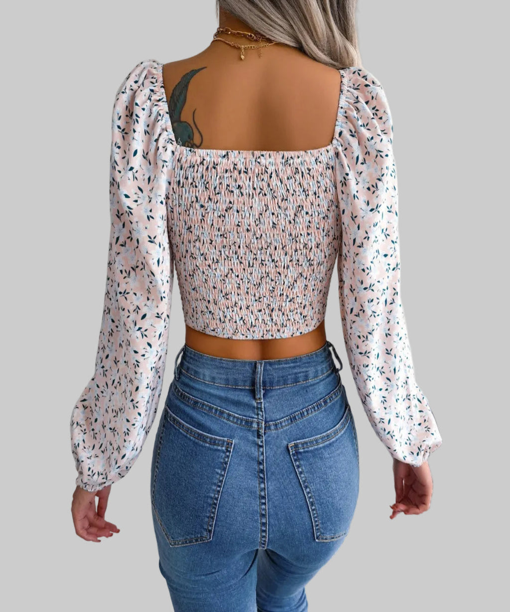 Person wearing a floral blouse with long sleeves and blue jeans on a neutral background