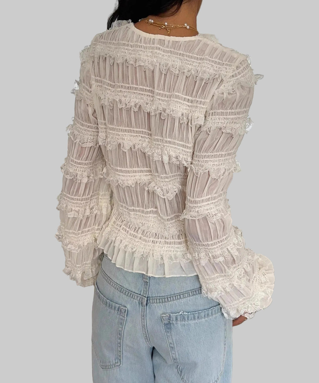 Person wearing a white lace top and light blue jeans indoors.