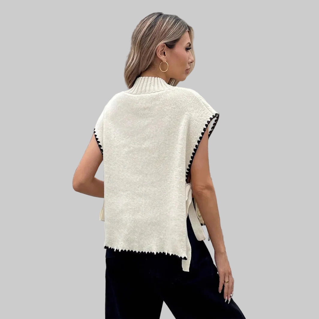 Woman wearing a white poncho with black trim walking on a crosswalk.