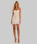 A woman stands on a white background wearing a white lace strapless mini dress with a corset-style bodice and sheer paneling. 