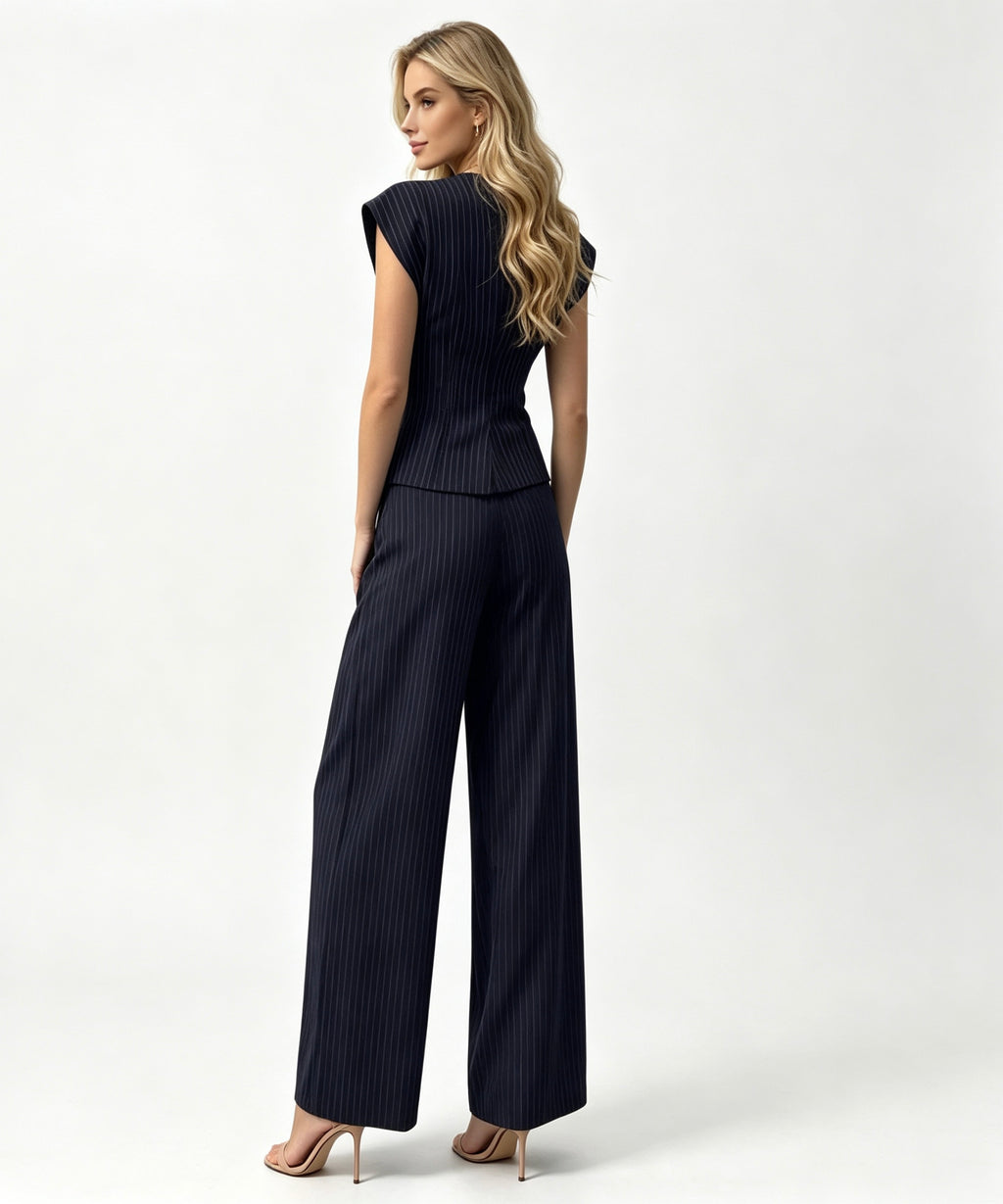 A woman modeling a dark navy pinstriped jumpsuit from the back, featuring a structured sleeveless bodice and wide-leg trousers, set against a plain white studio background.