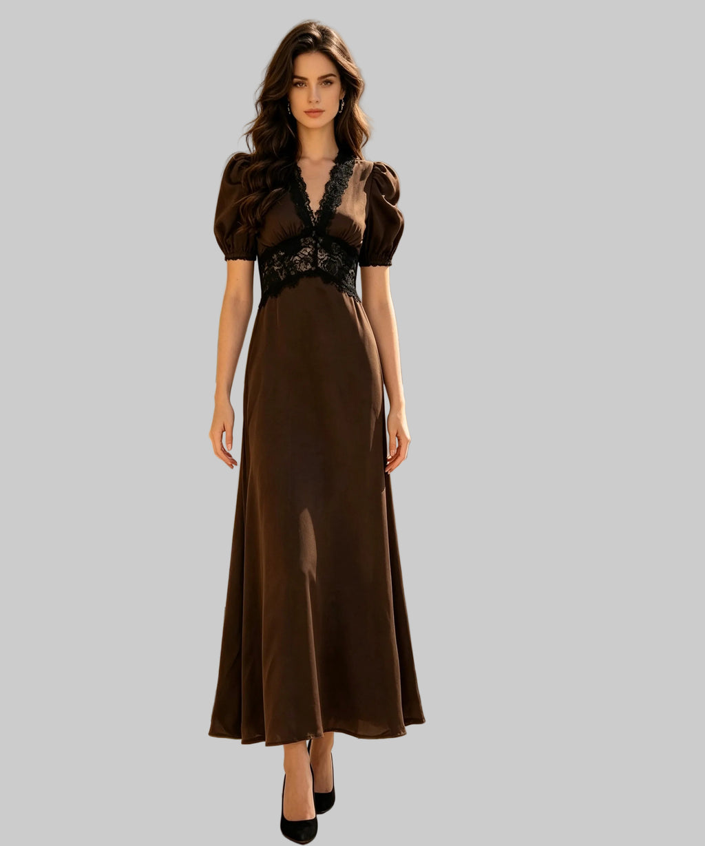 A woman stands on a white background wearing a long brown dress with puff sleeves, a deep V-neckline, and black lace detailing across the bodice. 