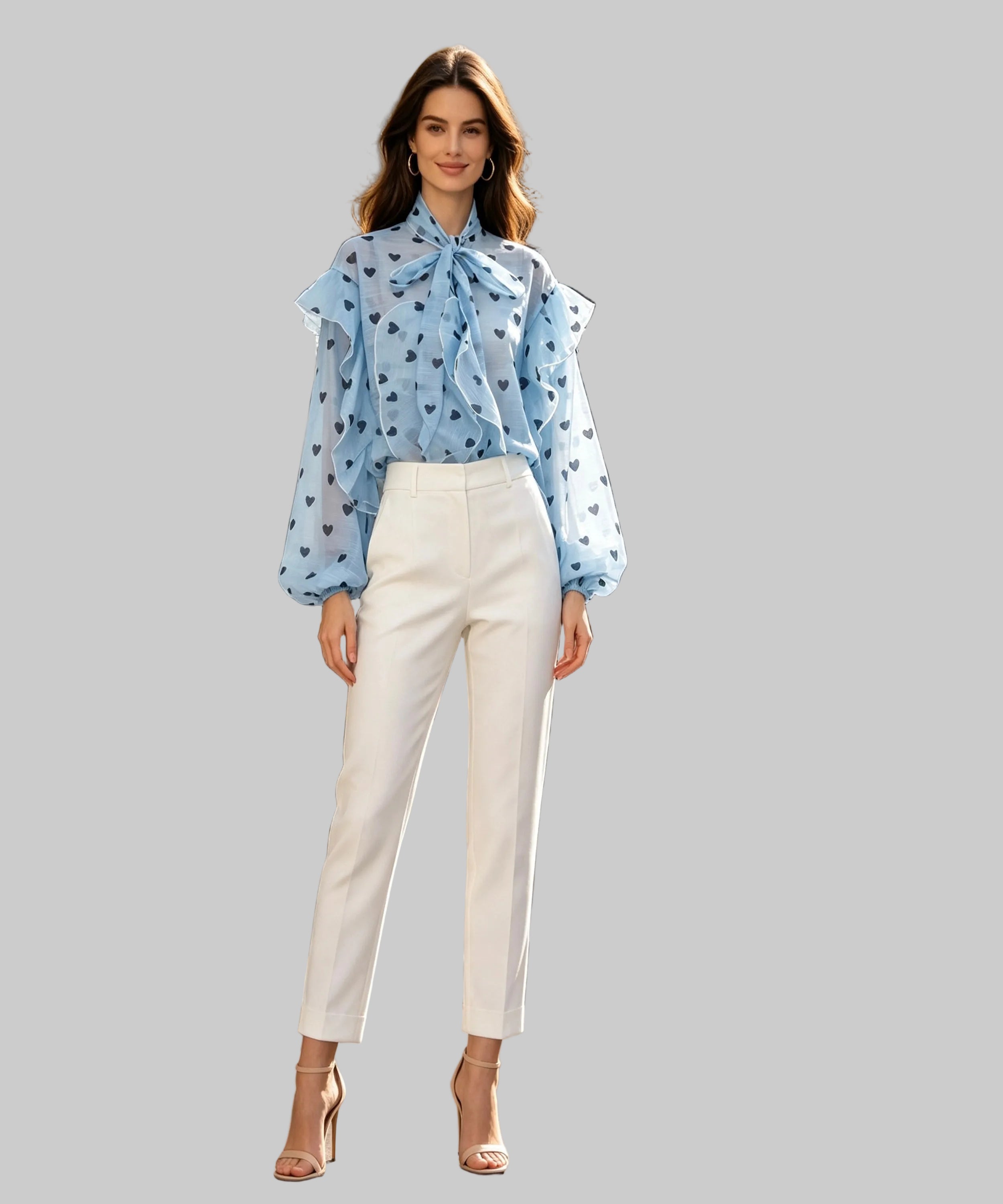 A woman stands on a white background wearing a light blue long-sleeve blouse with a bow tie neckline and small dark floral print, paired with white cropped pants and nude high-heel sandals. Storefronts and outdoor cafe seating are visible in the background.